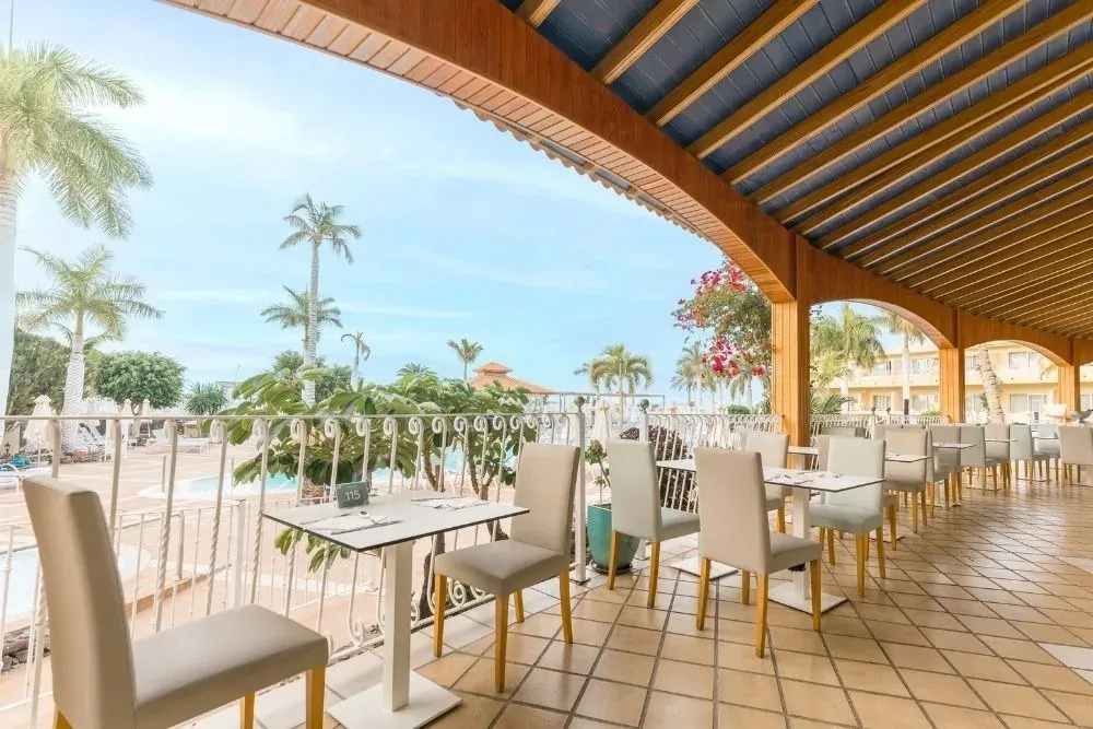 Comedor exterior en R2 Hoteles: Disfruta vistas a la piscina y palmeras.