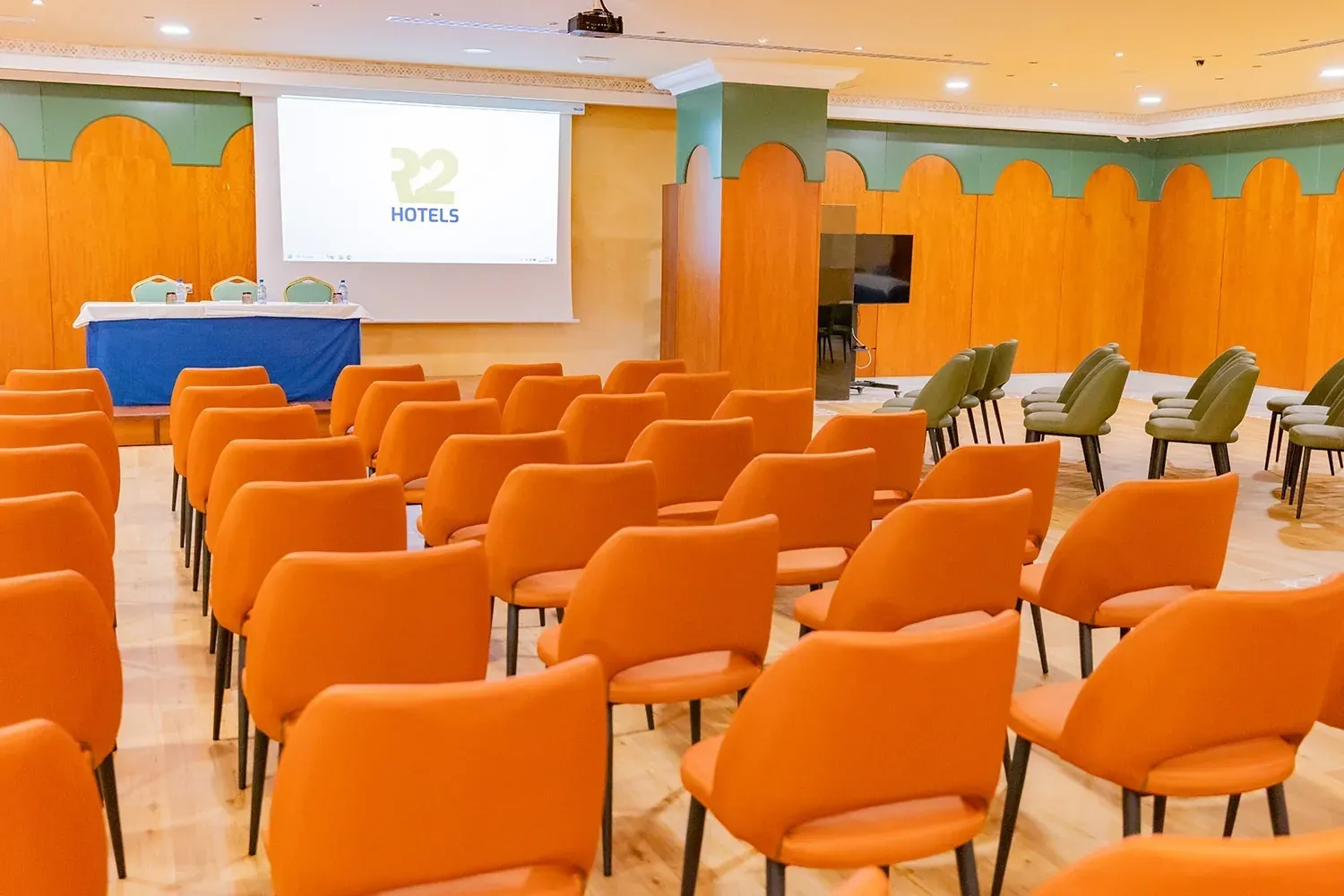 R2 Hotels Veranstaltungsraum: Orange und grüne Stühle, ideal für Firmenveranstaltungen.