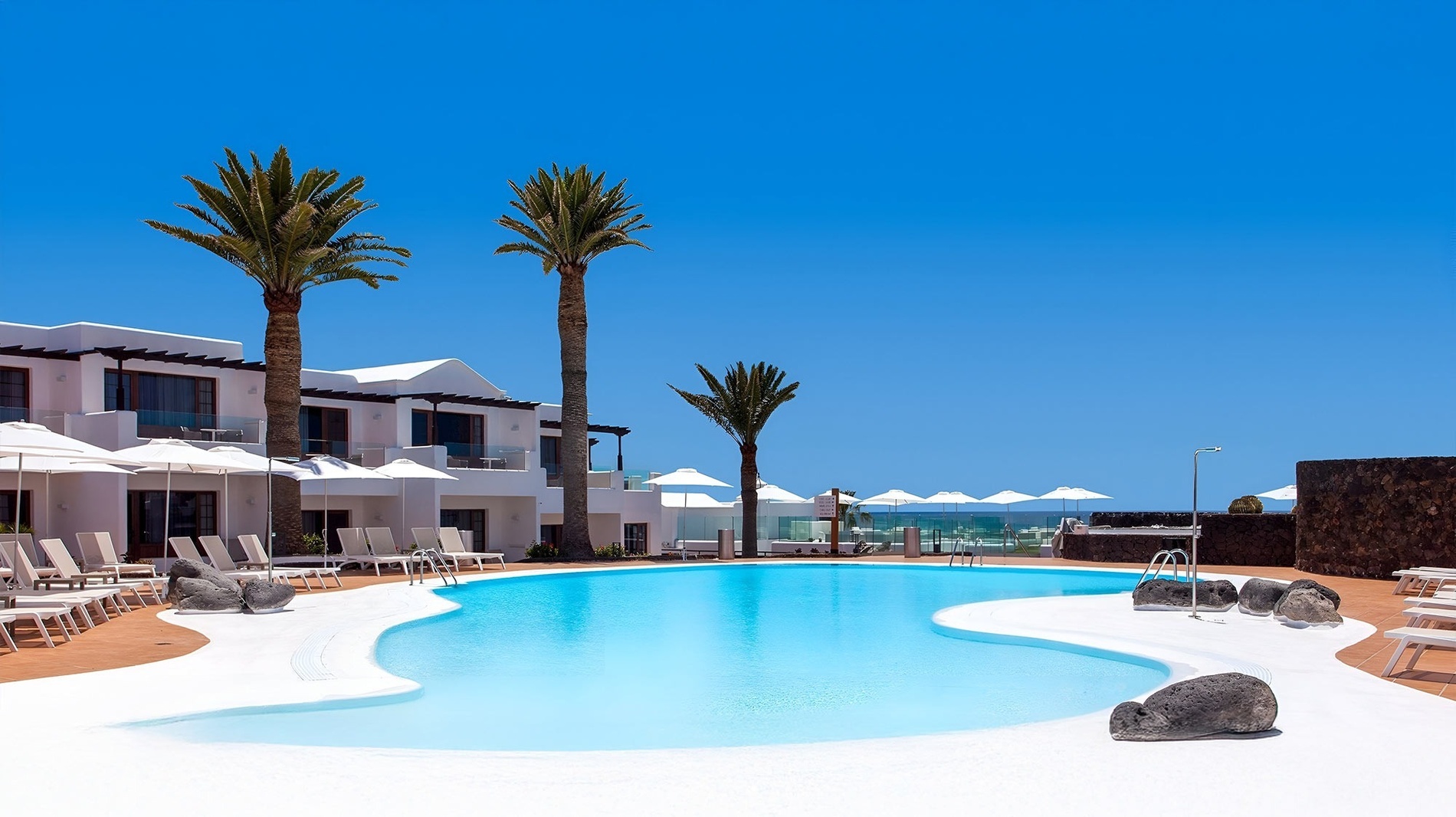 a large swimming pool surrounded by white chairs and umbrellas