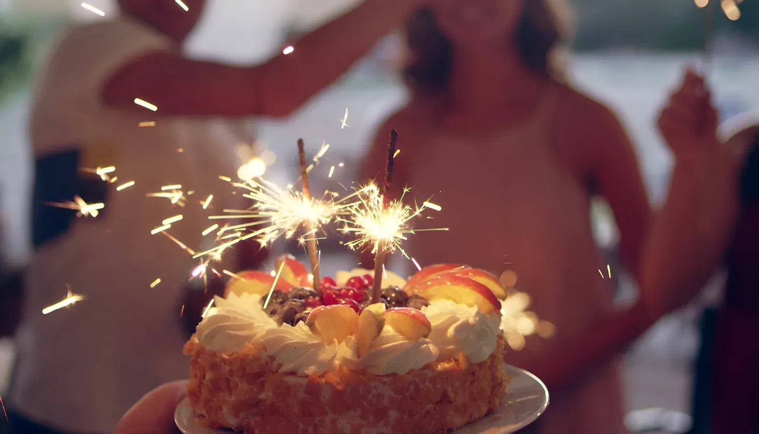 Gâteau d'anniversaire avec des étincelles et des gens qui célèbrent, idéal pour les événements d'entreprise R2 Hoteles.