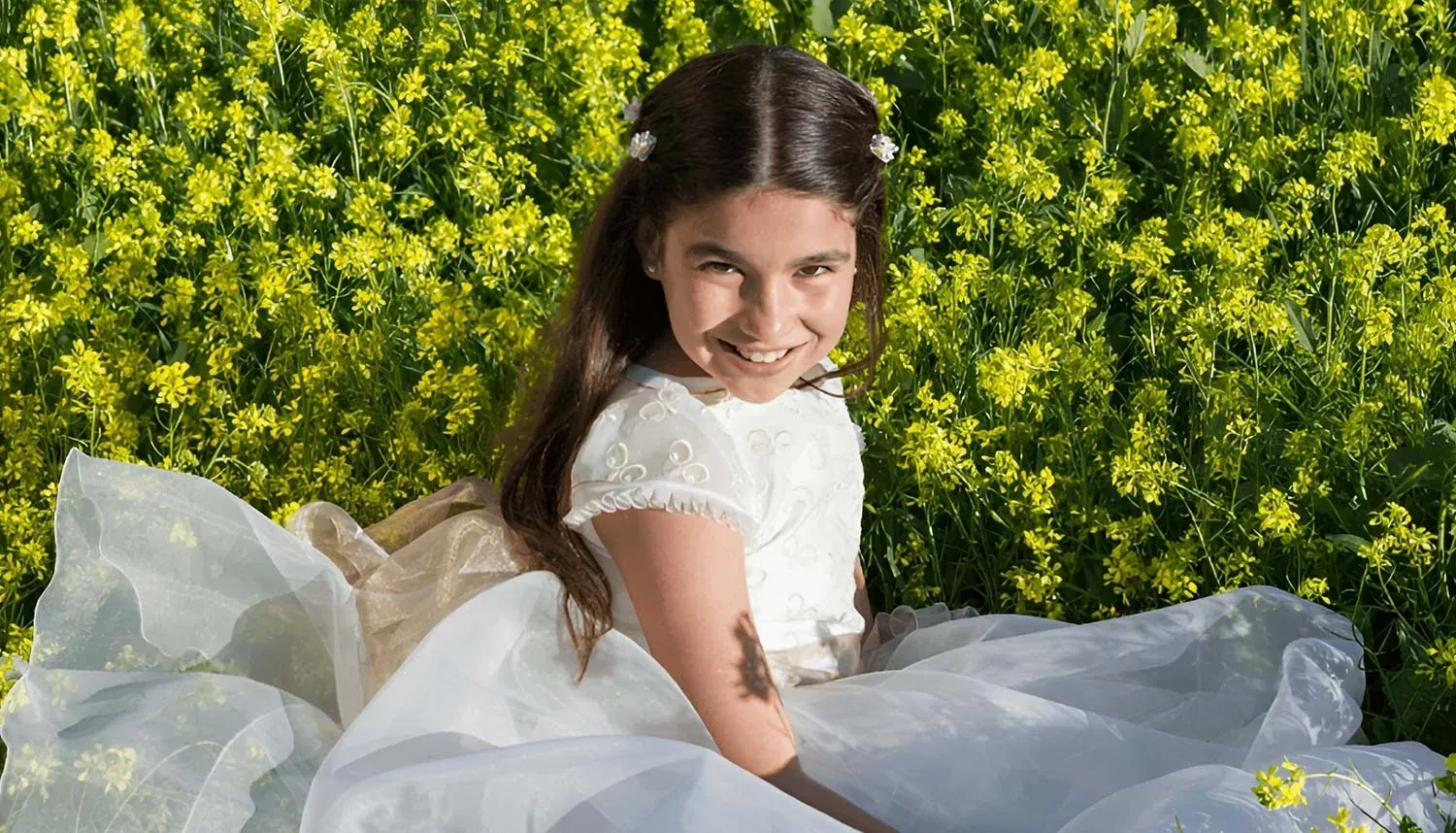 R2 Hotels : Petite fille en robe blanche souriant parmi les fleurs jaunes