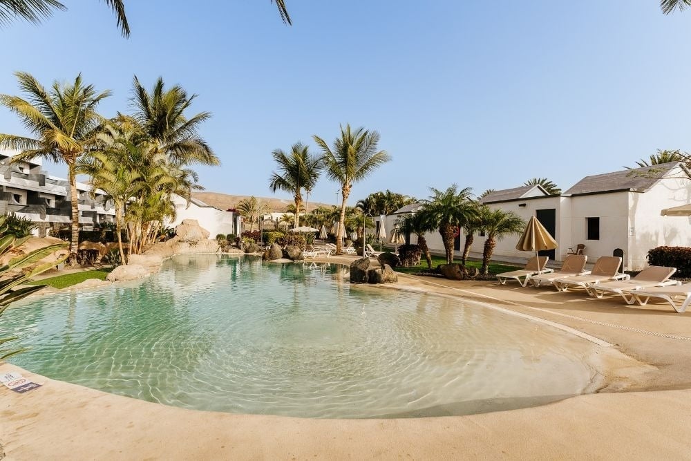Tropical pool with palm trees and lounge chairs at R2 Romantic Fantasia Dreams & Suites Hotel.