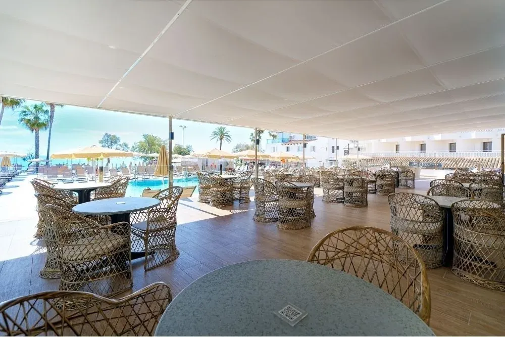 R2 Hoteles: Zona chill-out exterior con mesas y sillas de mimbre junto a la piscina.