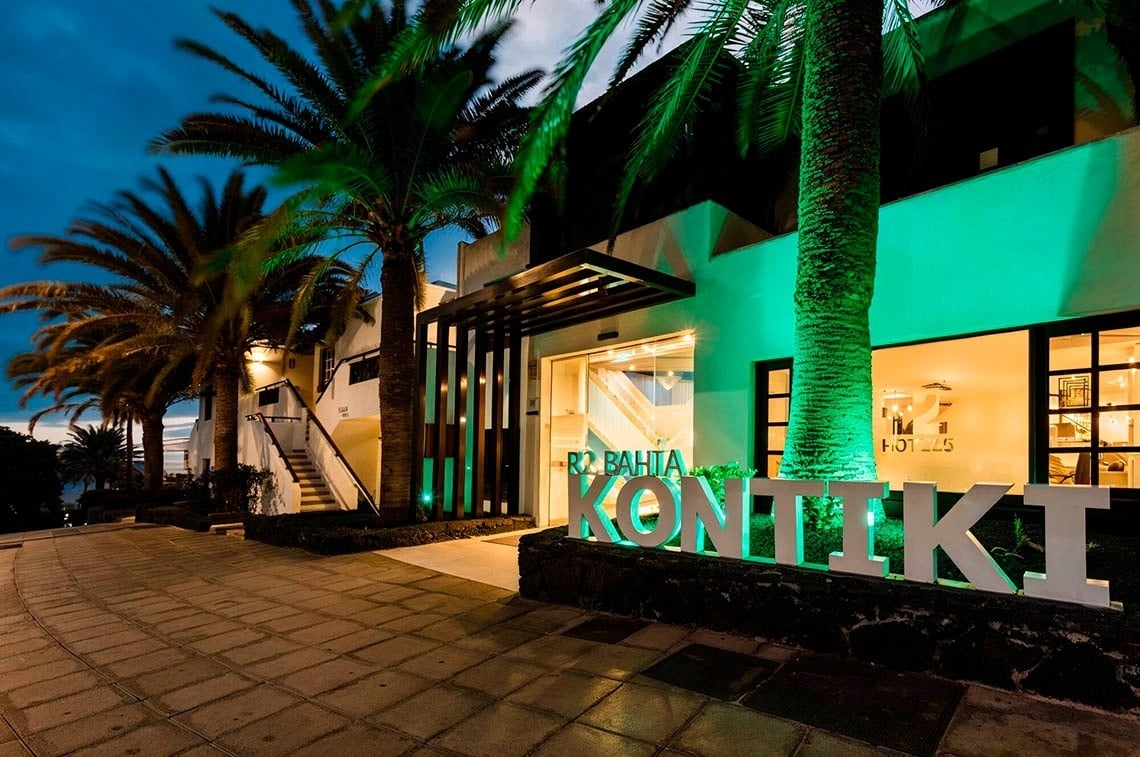 R2 Bahía Kontiki Beach Apartments | R2 Hotels & Residences: fachada iluminada con palmeras y cartel luminoso.