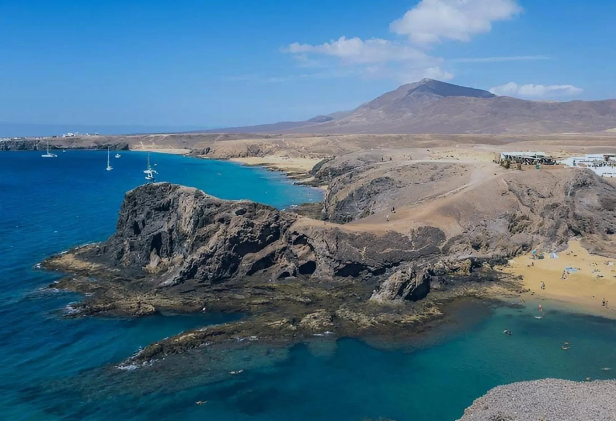 R2 Hoteles: Corporativa – Paisaje de playa volcánica con aguas claras.
