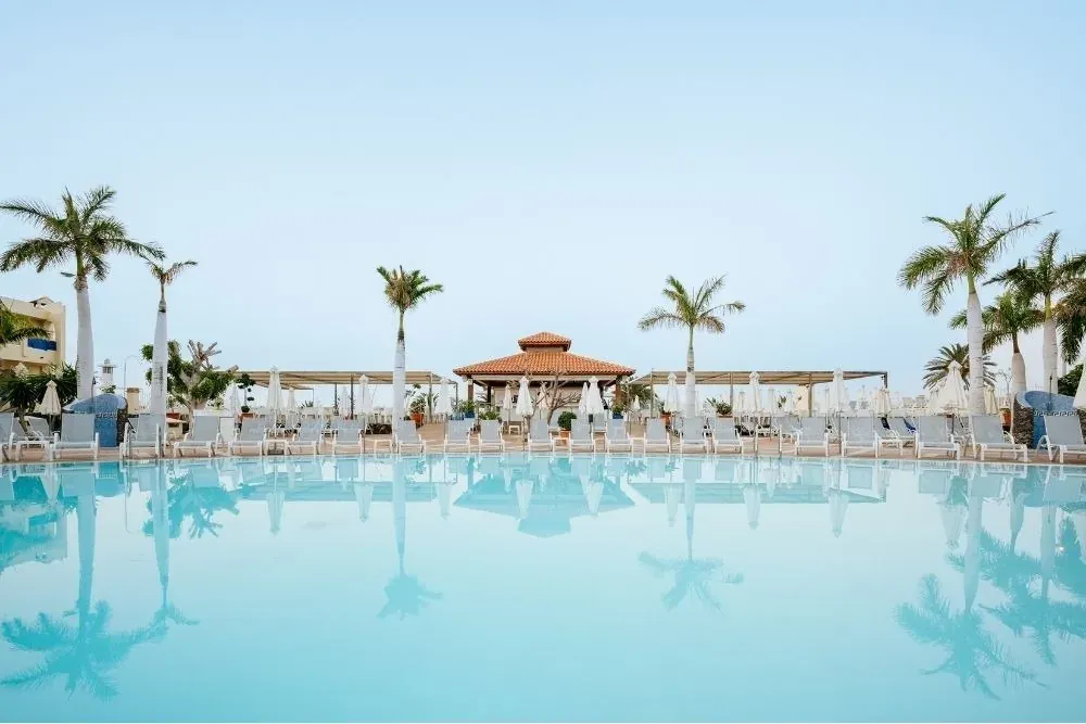Piscina R2 Hoteles: Corporativa, palmeras y tumbonas bajo el sol.