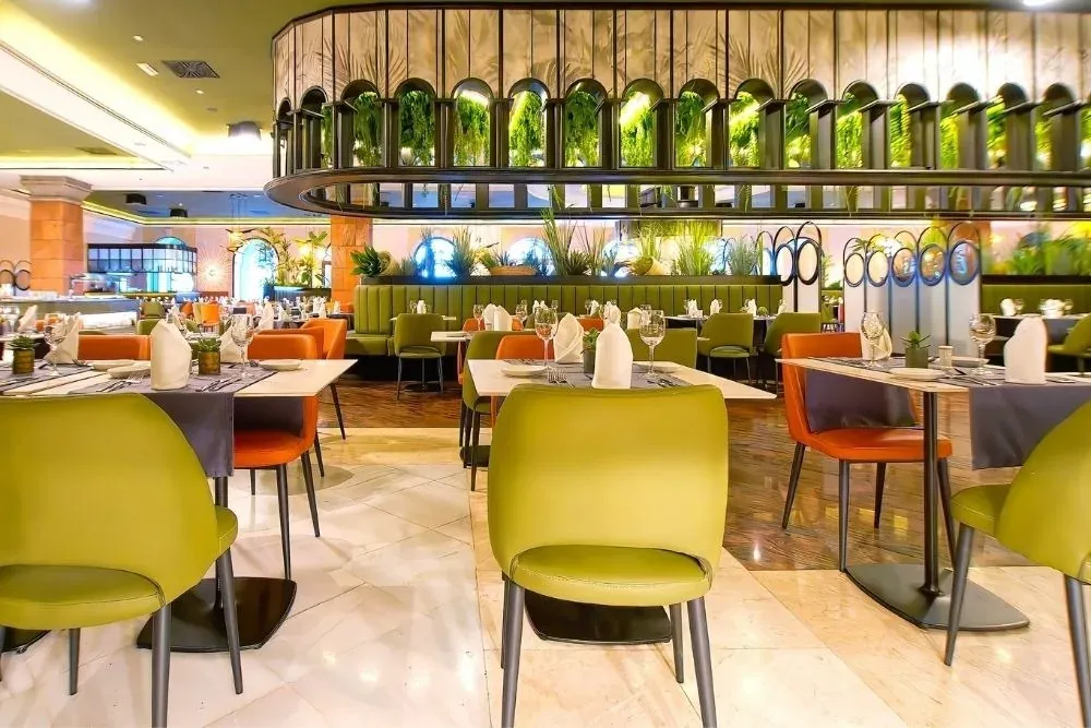 Ristorante aziendale R2 Hotels: Sala moderna con tavoli apparecchiati, sedie verdi e arancioni.