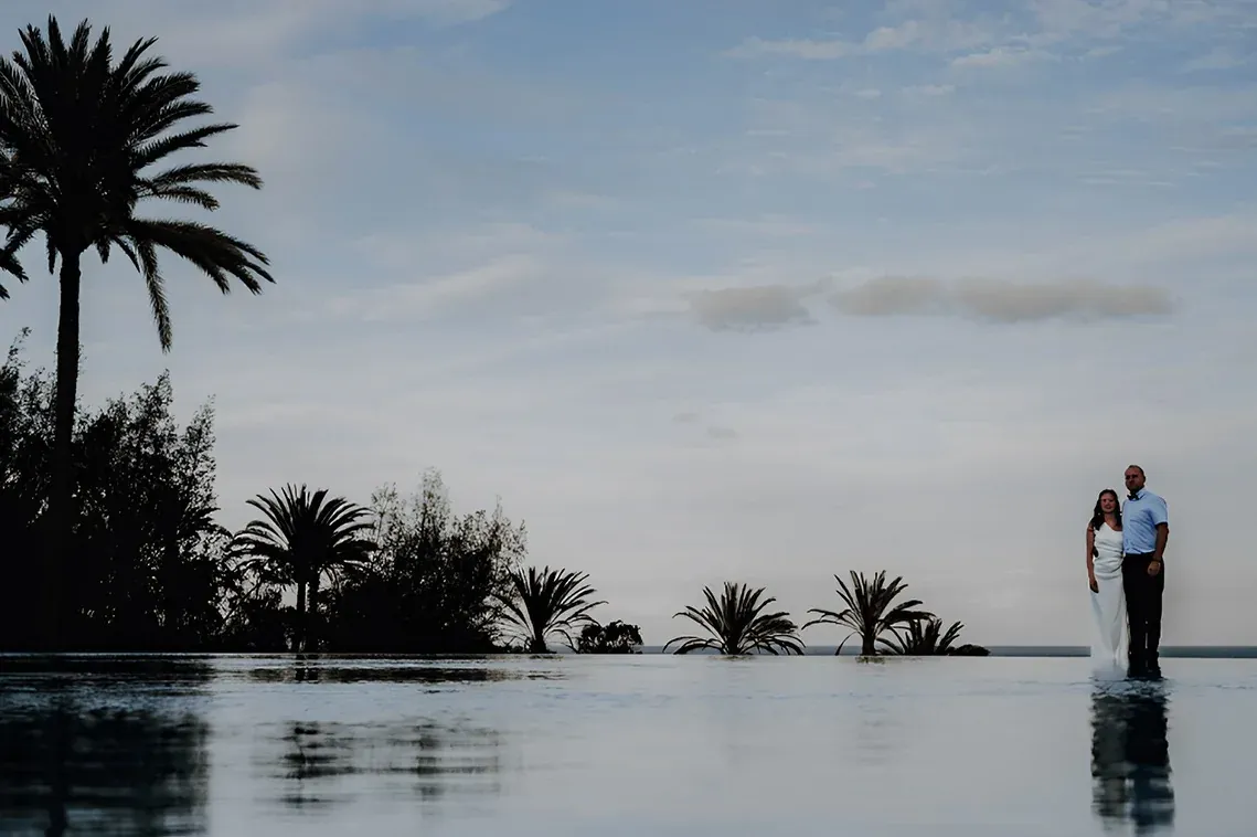 Pareja en piscina R2 Hoteles, vista al mar y palmeras.