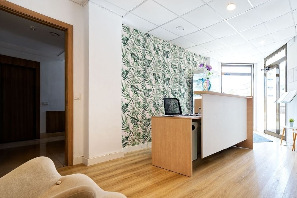 Réception moderne des appartements R2 Cala Millor Beach avec papier peint à feuilles et bureau en bois.