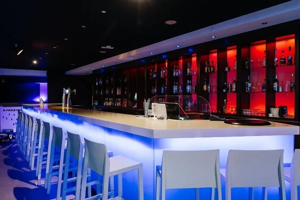 R2 Hoteles Corporativo: Bar moderno con iluminación LED azul y estantes de licores rojos.