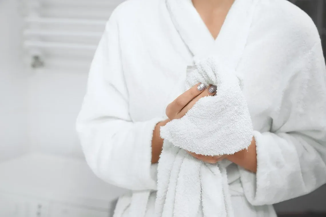 R2 Hoteles: Firmenkunde. Person im weißen Bademantel trocknet Hände mit Handtuch.