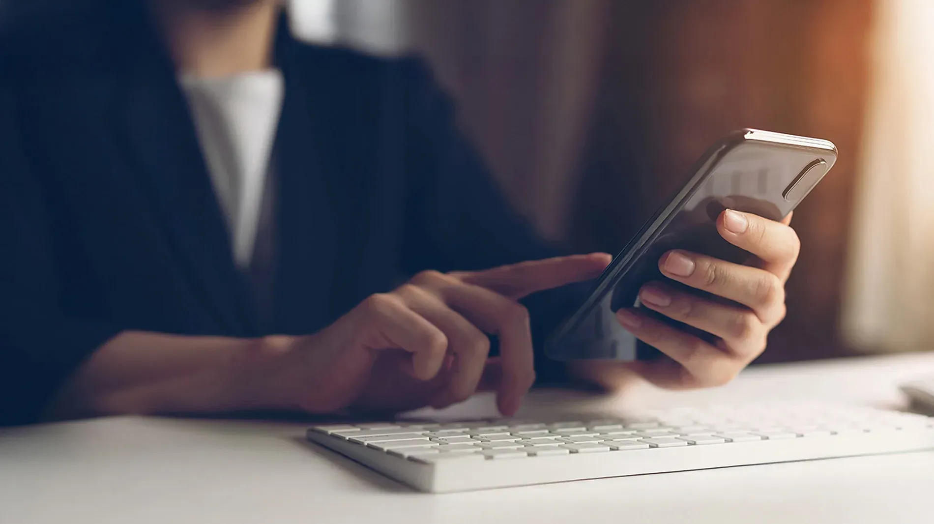 Persona usando smartphone en escritorio con teclado. Contacto | R2 Hotels | Web Oficial.
