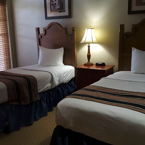 Two twin beds in a Travel Raintree Corpo hotel room with decorative throws and nightstand.