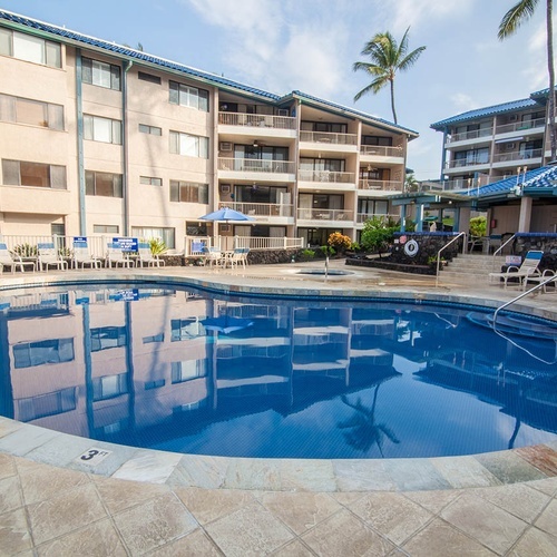Sparkling pool at Travel Raintree Corpo, surrounded by buildings and palm trees.