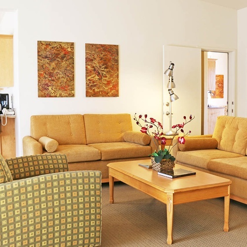 Comfortable living room with gold sofas and abstract art for your Travel Raintree Corpo stay.