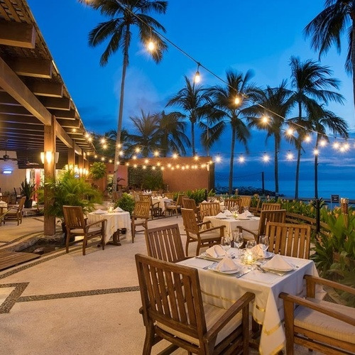 Travel Raintree Corpo: Elegant al fresco dining with ocean views and palm trees at dusk.