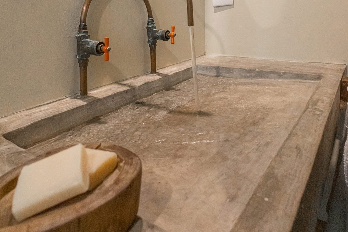 a bathroom sink with two faucets and a wooden bowl of soap