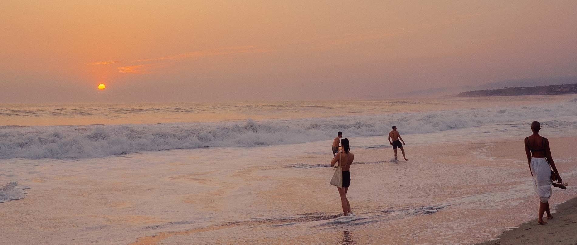 a group of people standing on a beach at sunset