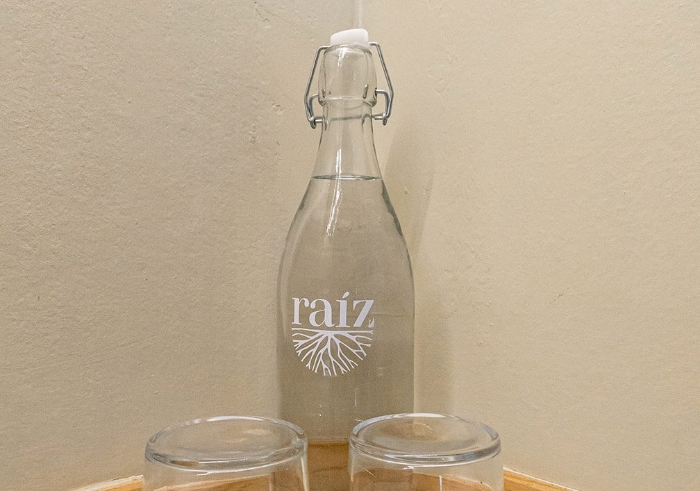 a bottle of raiz sits next to two empty glasses