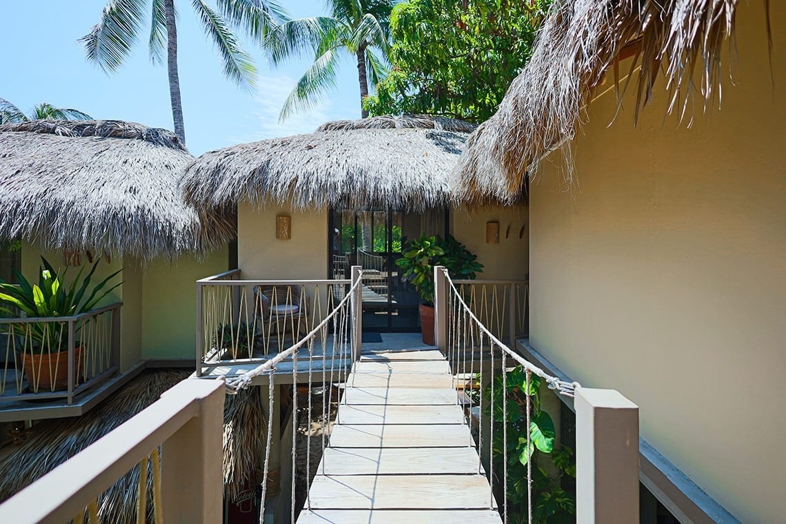 a rope bridge between two buildings with thatched roofs