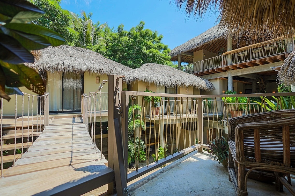 a wooden bridge between two buildings with thatched roofs