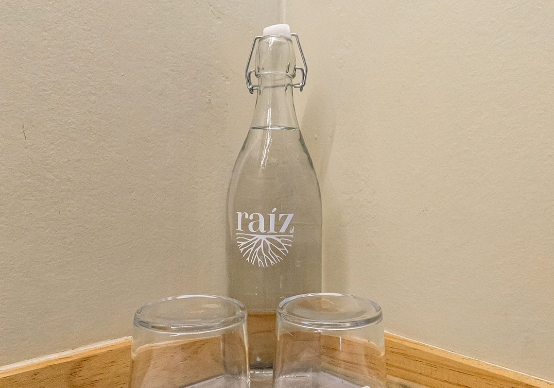 a bottle of raiz sits next to two empty glasses