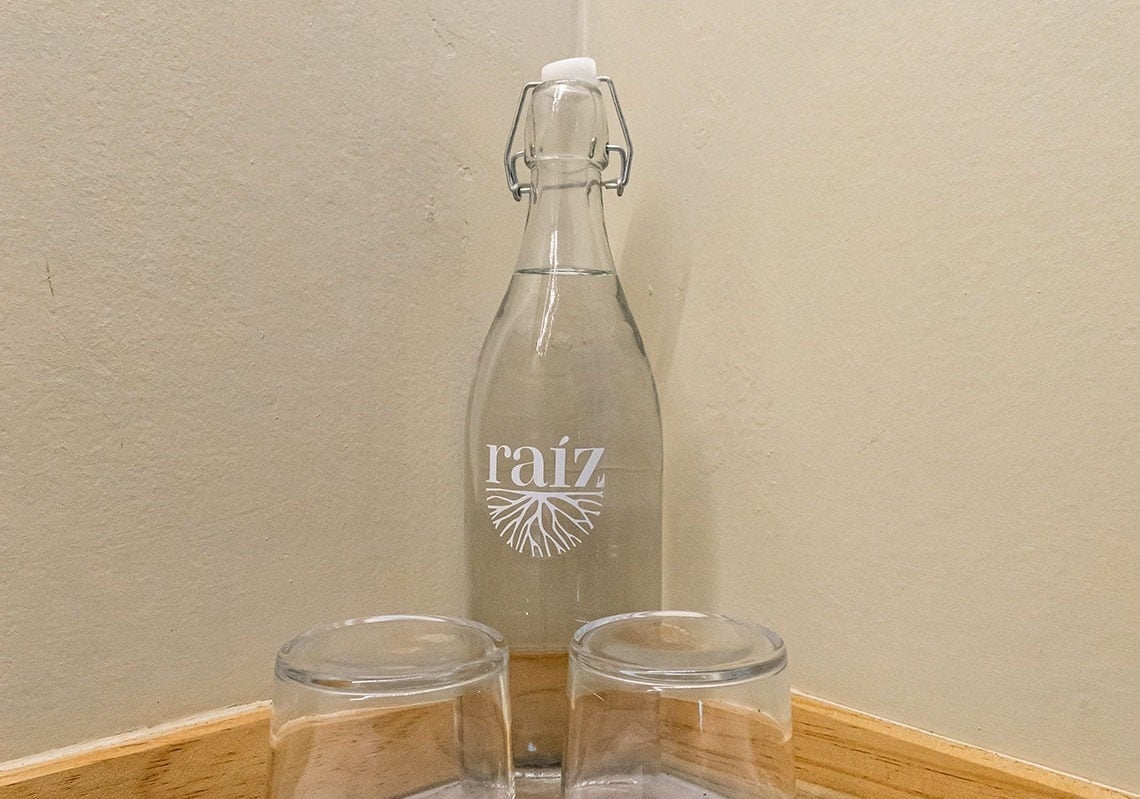 a bottle of raiz sits next to two empty glasses