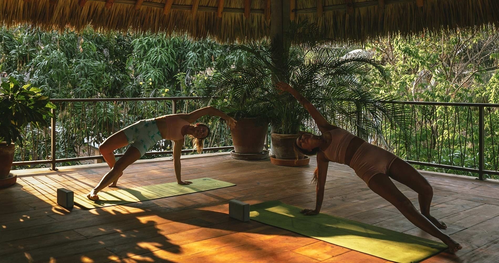 dos mujeres hacen yoga en una terraza con techo de paja