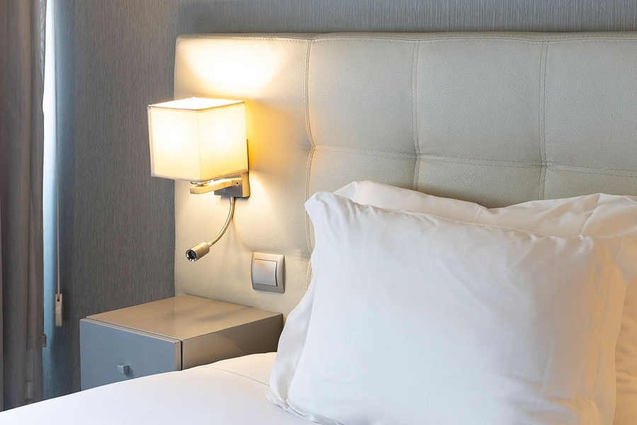 a bed with white pillows and a lamp on the wall