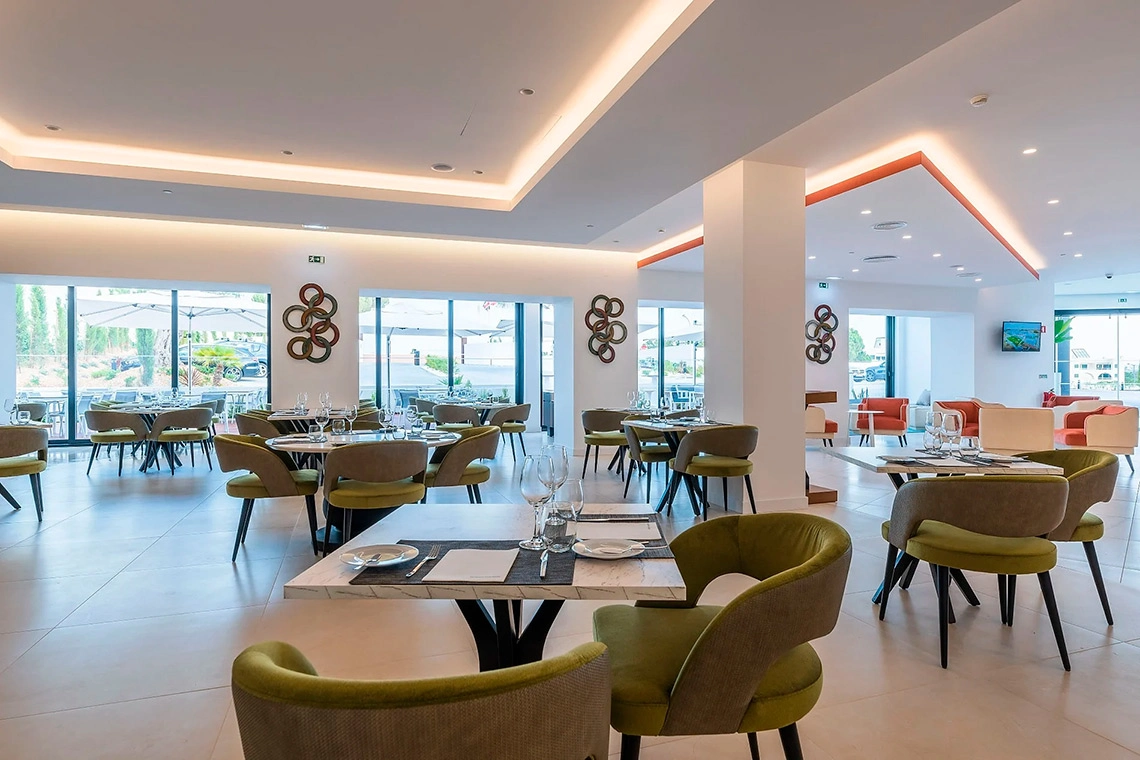Salão de jantar sofisticado no Regency Salgados, com mesas postas e cadeiras verdes.