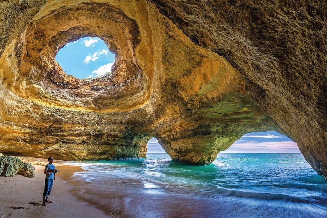 a man stands on a beach in a cave looking out at the ocean