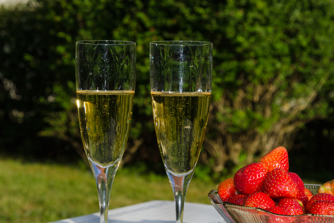 Dos copas de champán con fresas y elRegency Salgados en un jardín soleado.