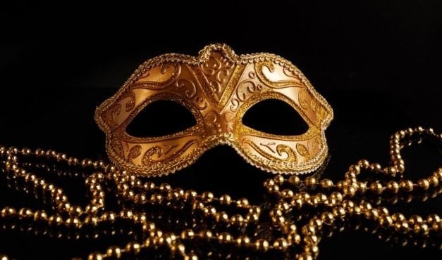 a gold mask is sitting on top of a string of gold beads on a black background .