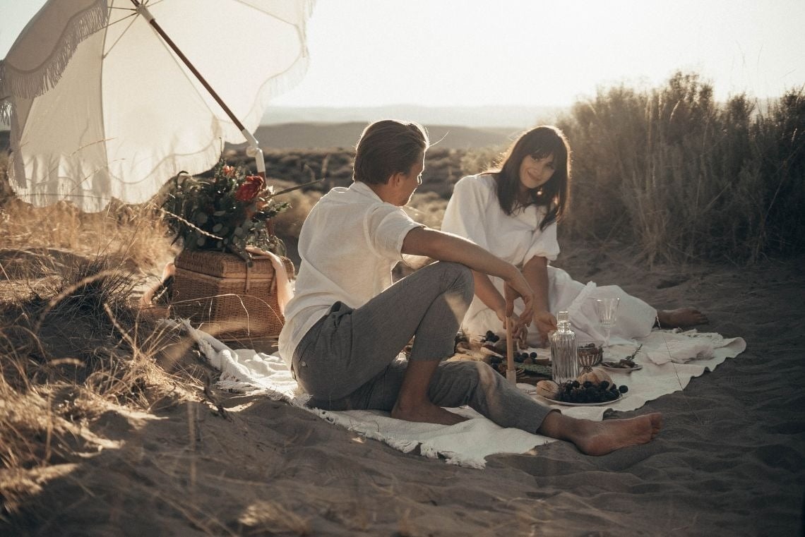 a man and a woman are sitting on a blanket on the beach