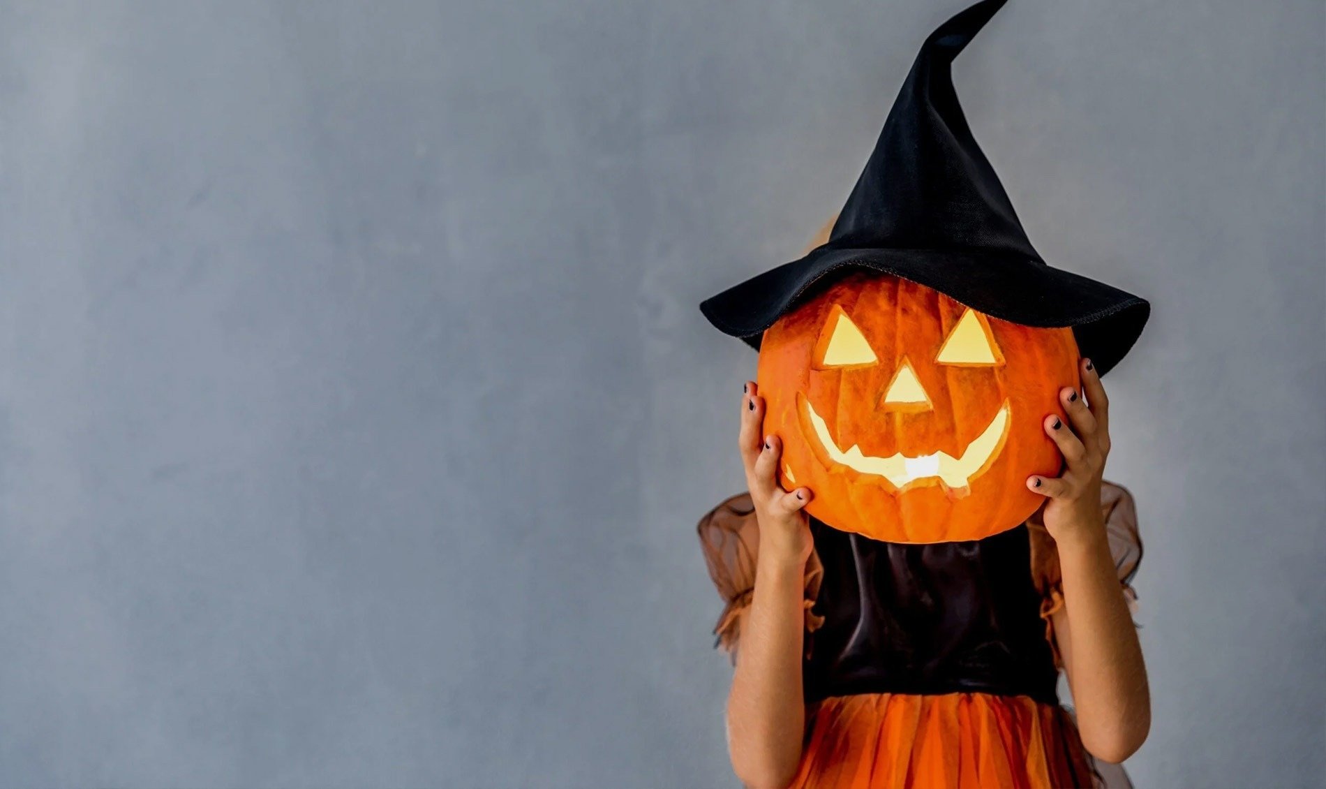 una niña con un sombrero de bruja sostiene una calabaza frente a su cara