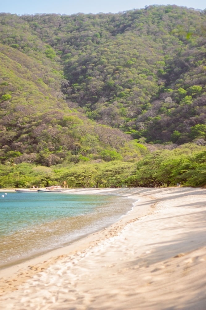 Playa tropical junto a colinas verdes, ideal para tu estancia en Hotel Ribai Corporativa.