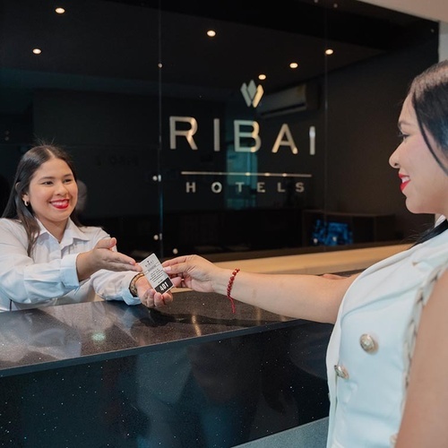Recepcionista de Hotel Ribai entrega tarjeta de habitación a huésped.