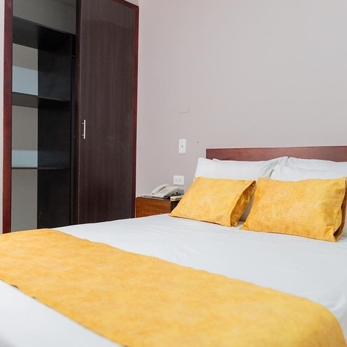 Cama matrimonial con cojines amarillos en Hotel Ribai Corporativa.
