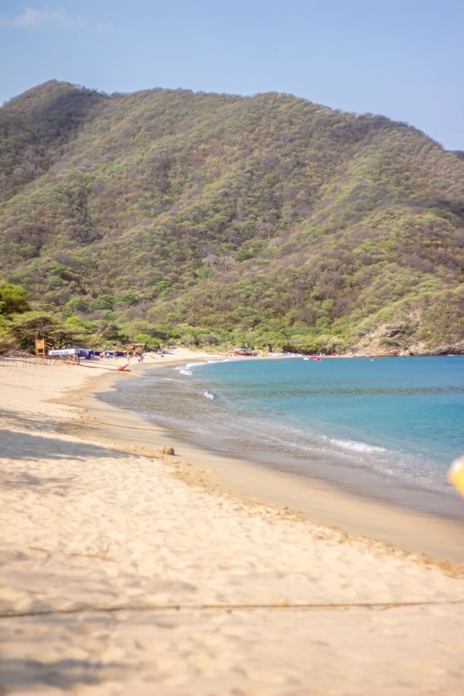 Playa paradisíaca con montaña verde y mar azul, ideal para relajarse en Hotel Ribai Corporativa.
