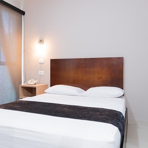 Habitación limpia y moderna en Hotel Ribai Corporativa con cama cómoda y mesa de noche.