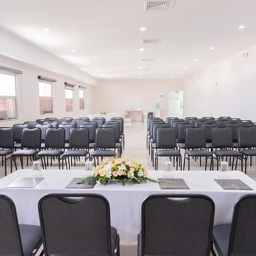 Salón de eventos del Hotel Ribai Corporativa con sillas dispuestas y mesa de flores.