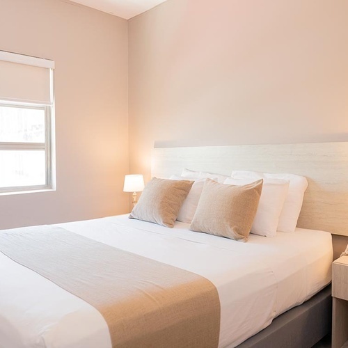 Cama cómoda en Hotel Ribai Corporativa con almohadas, lámpara y mesa de noche.