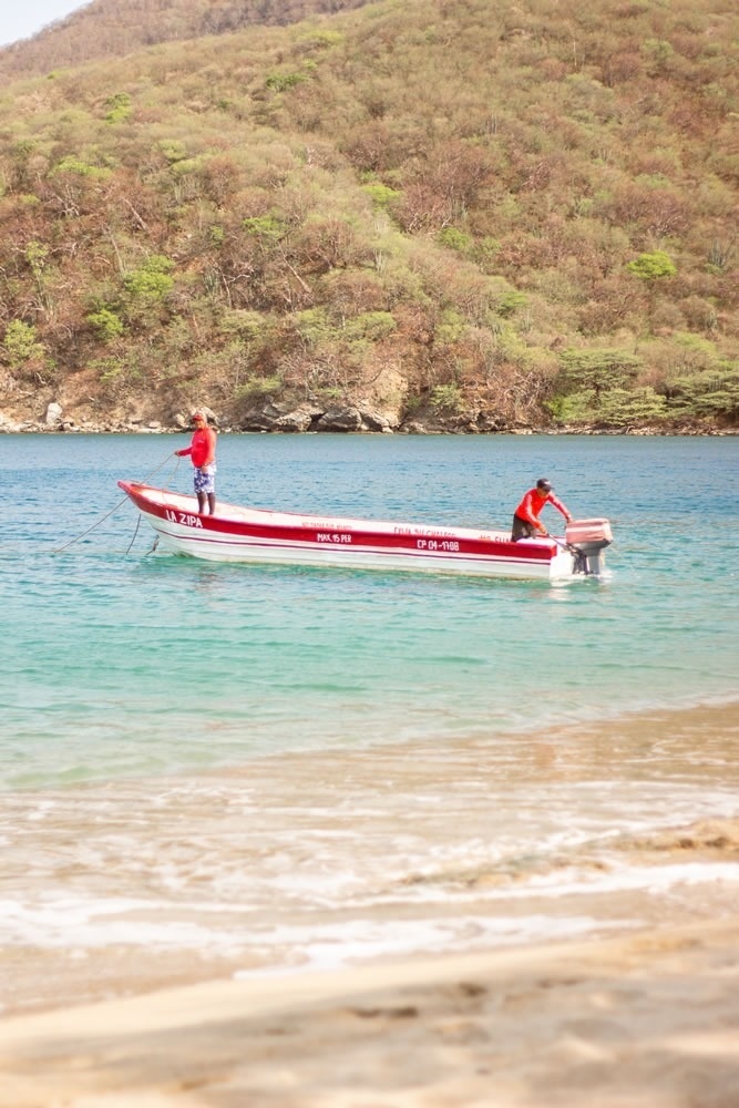 Barco rojo con personas, fondo de montaña y playa. Hotel Ribai Corporativa.