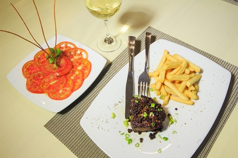 Exquisito plato de carne con patatas fritas y ensalada de tomate en Hotel Ribai Corporativa.