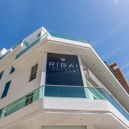 Hotel Ribai Corporativa moderno con fachada blanca y balcón de cristal.
