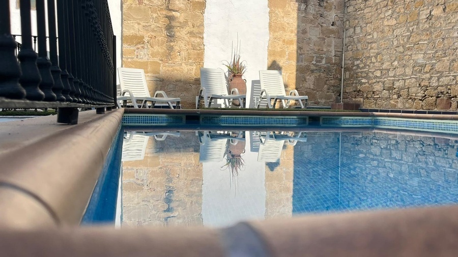 una piscina rodeada de sillas y sombrillas frente a un edificio blanco