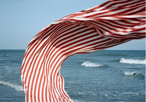 Una tela a rayas rojas y blancas ondea sobre el mar azul con olas.