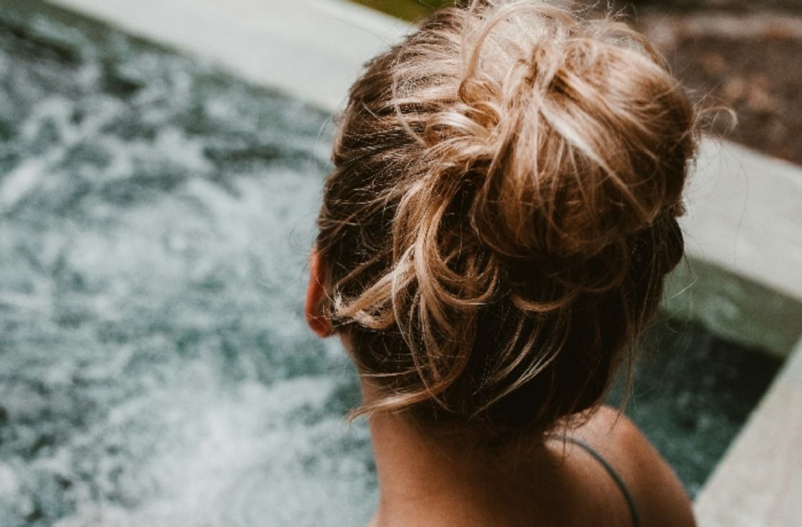 Una persona de espaldas con el pelo recogido en un moño se encuentra junto a un cuerpo de agua burbujeante.