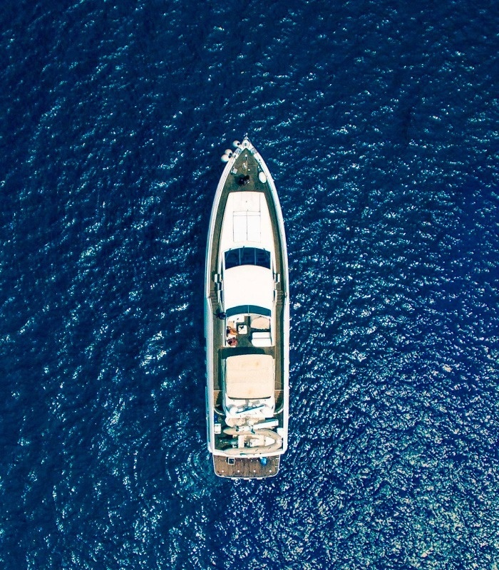 An aerial top-down view shows a white yacht floating on deep blue, rippling water.