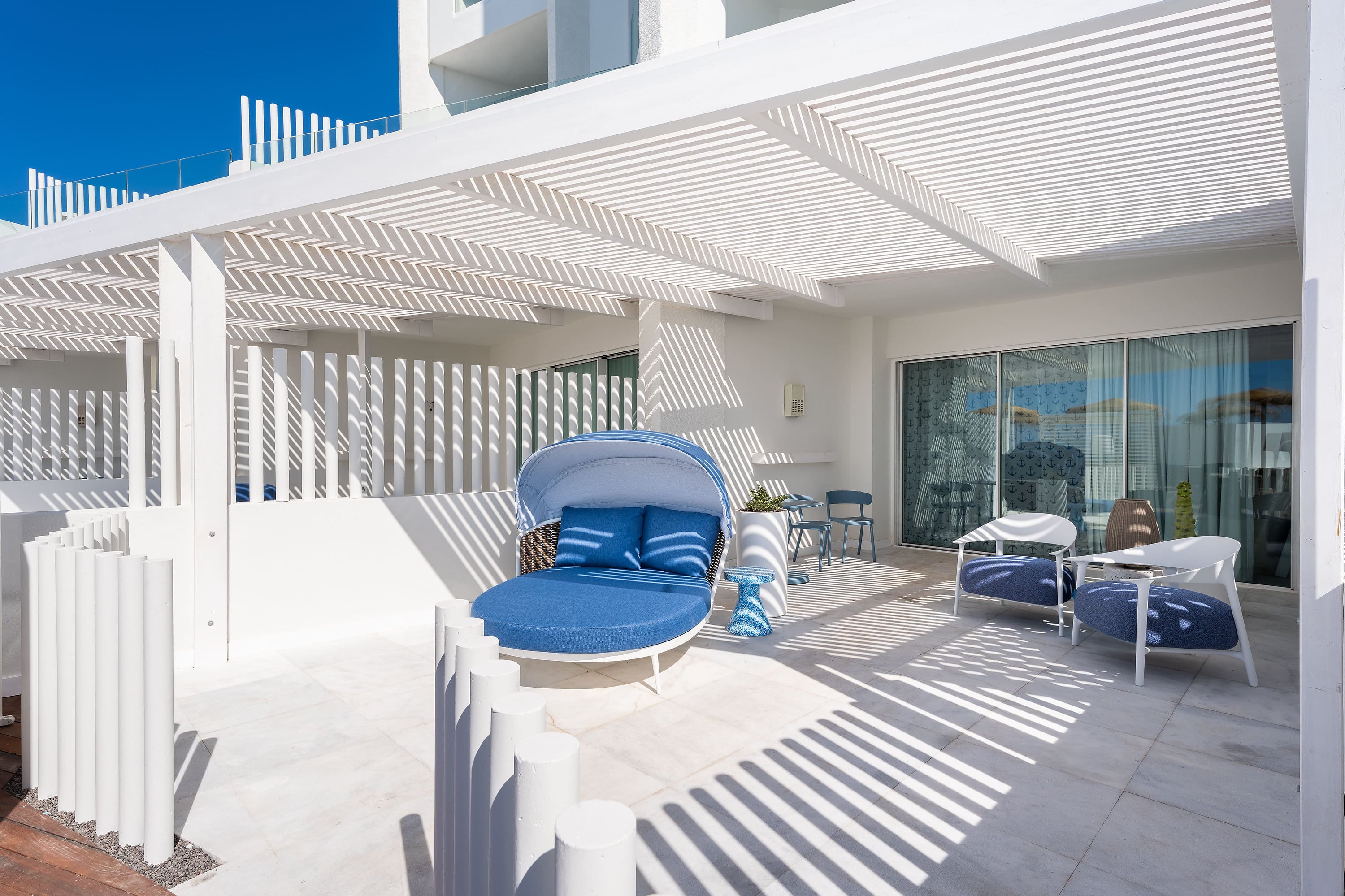 Terraza de hotel moderna con tumbona azul, sillas blancas y sombras de listones, ideal paraSatocan: The Salmar.